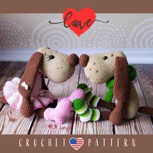 Puede incluir: Dos peluches de perro de crochet, uno con un tutú rosa y el otro con una bufanda verde, se besan. La palabra "love" está escrita encima de ellos en rojo con una huella de pata en el medio del corazón.