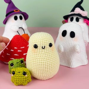 Puede incluir: Un grupo de juguetes de crochet con tem&aacute;tica de Halloween, que incluyen fantasmas, un hongo y dos ranas verdes. Los fantasmas llevan sombreros de bruja y tienen caras lindas. El hongo es rojo con manchas blancas. Las ranas son verdes con ojos negros y caras sonrientes.