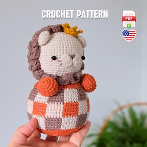 Puede incluir: Patrón de crochet para un león con una corona. El león es marrón y naranja con un patrón a cuadros en su cuerpo. El patrón está disponible para descargar en PDF.