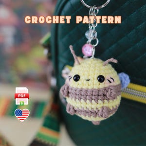 Puede incluir: Patrón de crochet para un llavero de abeja lindo. La abeja es amarilla y marrón con ojos negros y una nariz rosa. El patrón está disponible para descargar en PDF.