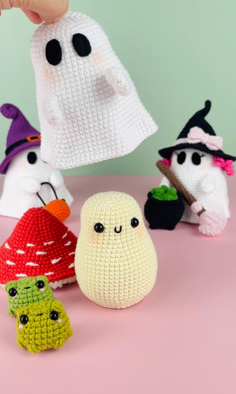 Puede incluir: Una colecci&oacute;n de juguetes de ganchillo con tem&aacute;tica de Halloween, que incluye un fantasma, una bruja, un hongo y dos ranas. Los juguetes est&aacute;n hechos con hilo blanco, verde, rojo y morado.