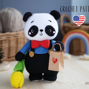Può includere: Schema all'uncinetto per un giocattolo amigurumi panda che tiene una busta di carta marrone con un cuore rosso. Il panda indossa una camicia blu con un papillon rosso e una salopette nera. Il panda tiene un tulipano giallo.