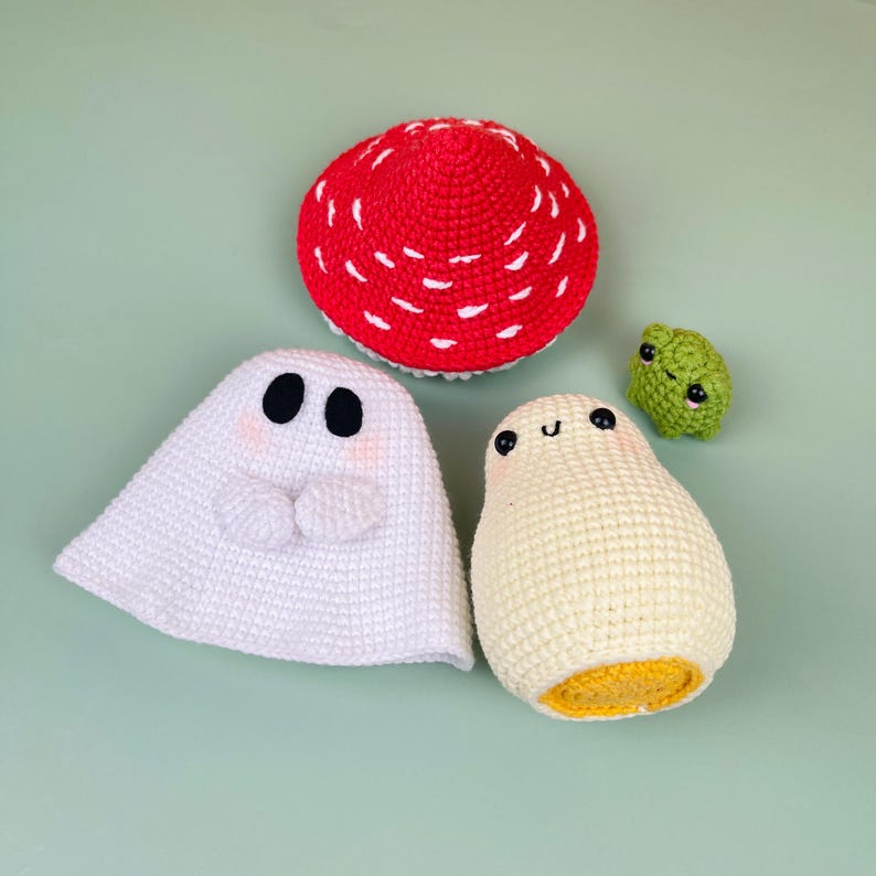 Puede incluir: Un conjunto de cuatro juguetes amigurumi de crochet: un fantasma blanco, un huevo amarillo, una seta roja y blanca y una rana verde.