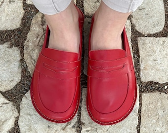 May include: A pair of red leather loafers with a simple design. The loafers have a rounded toe and a stitched seam around the edge.