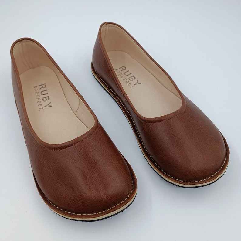 Peut inclure: Une paire de ballerines en cuir marron avec le texte "RUBY BAREFOOT" imprim&eacute; sur la semelle int&eacute;rieure. Les chaussures ont un bout arrondi, une semelle cousue et une semelle de couleur neutre.