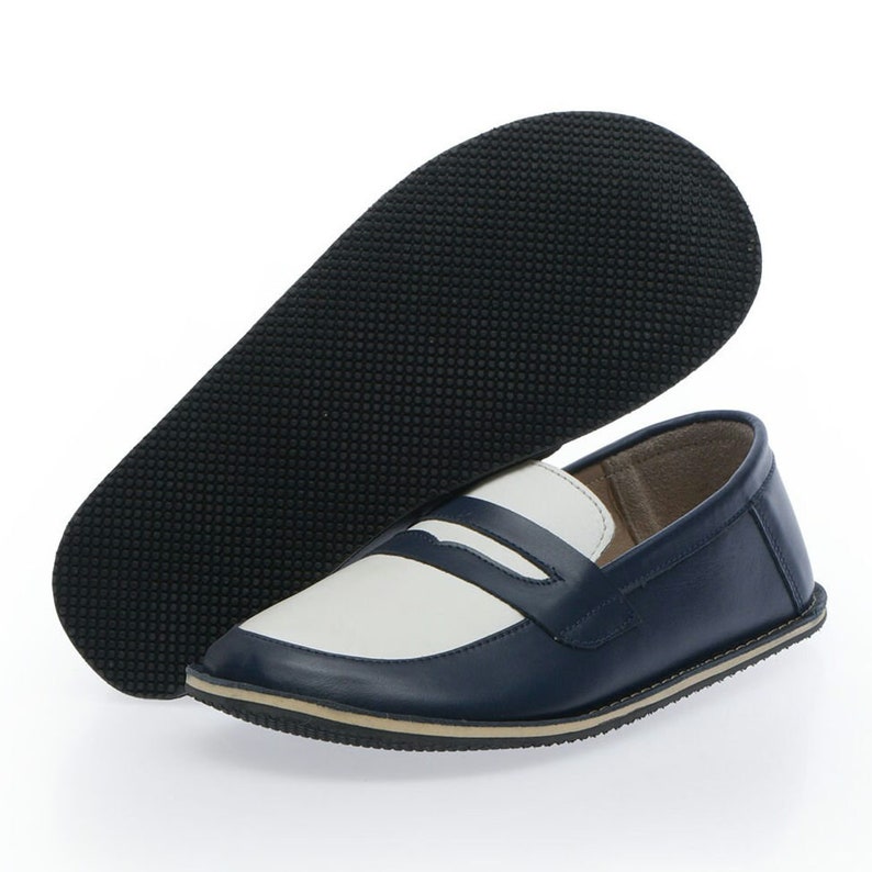 May include: A pair of blue and white leather loafers with a black rubber sole. The loafers have a white leather upper with a blue leather trim and a blue leather strap across the top.