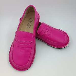 Peut inclure: Une paire de mocassins en cuir rose avec un logo "RUBY BAREFOOT" &agrave; l'int&eacute;rieur de la chaussure gauche.