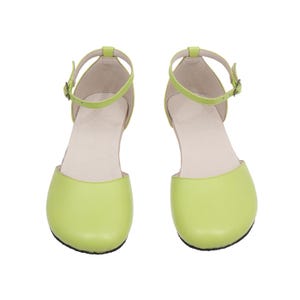 Puede incluir: Un par de bailarinas verde lima con correas en el tobillo y peque&ntilde;as hebillas. Los zapatos tienen una punta redondeada y un tac&oacute;n bajo. Las correas y el cuerpo del zapato son del mismo color. El interior del zapato es de color beige claro.