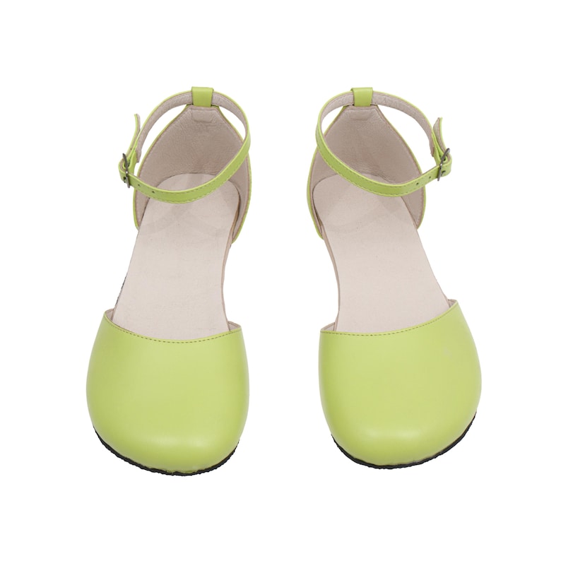 Puede incluir: Un par de bailarinas verde lima con correas en el tobillo y peque&ntilde;as hebillas. Los zapatos tienen una punta redondeada y un tac&oacute;n bajo. Las correas y el cuerpo del zapato son del mismo color. El interior del zapato es de color beige claro.