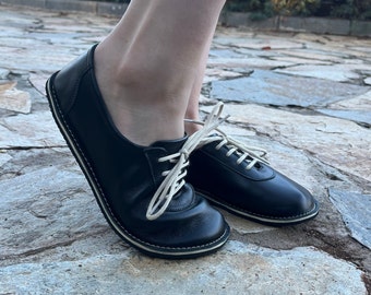 May include: A pair of black leather lace-up shoes with white laces. The shoes have a white stitching detail around the sole.