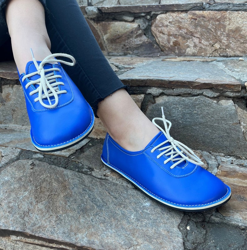 May include: A pair of blue leather lace-up shoes with white laces and a white trim around the sole.