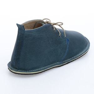 May include: A blue leather ankle boot with a lace-up closure. The boot has a cream-coloured sole and a slightly pointed toe.