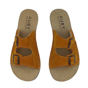 Könnte beinhalten: Senfgelbe Wildledersandalen mit zwei verstellbaren Schnallen. Die Sandalen haben ein Korkfußbett und der Text "RUBY BAREFOOT" ist auf der Innensohle aufgedruckt. Für Komfort konzipiert, ideal für den lässigen Gebrauch.