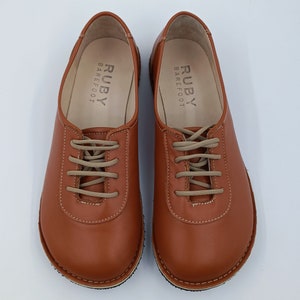 May include: A pair of brown leather lace-up shoes with the text "RUBY BAREFOOT" on the inside of each shoe.