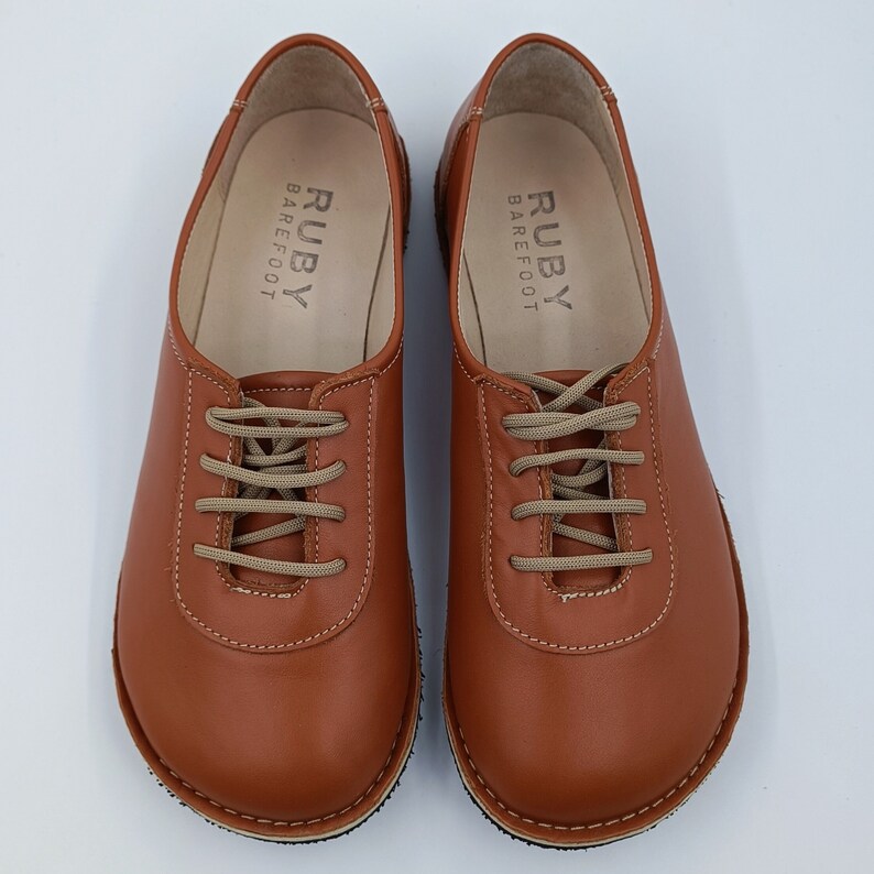 May include: A pair of brown leather lace-up shoes with the text "RUBY BAREFOOT" on the inside of each shoe.