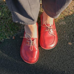 May include: A pair of red leather lace-up shoes with beige laces. The shoes have a rounded toe and a slightly raised heel.