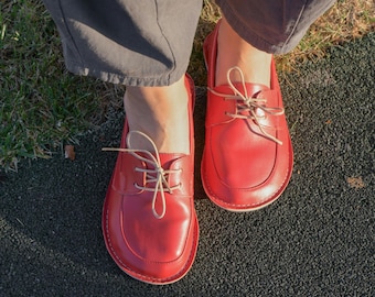May include: A pair of red leather lace-up shoes with beige laces. The shoes have a rounded toe and a slightly raised heel.