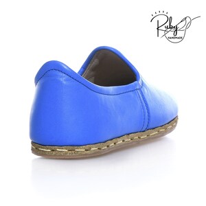 K&ouml;nnte beinhalten: Ein Paar blaue Lederschuhe zum Hineinschl&uuml;pfen mit einer braunen, gen&auml;hten Sohle. Die Schuhe sind handgefertigt und haben ein schlichtes, elegantes Design.