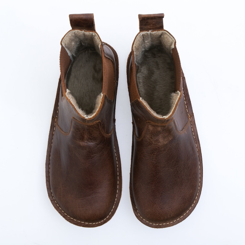Puede incluir: Un par de botines de cuero marr&oacute;n con forro de ante. Las botas tienen una puntera redonda y un estilo de calcet&iacute;n.
