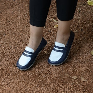 May include: A pair of white and navy blue leather loafers with a contrasting color design. The loafers have a simple, classic style and are perfect for casual wear.