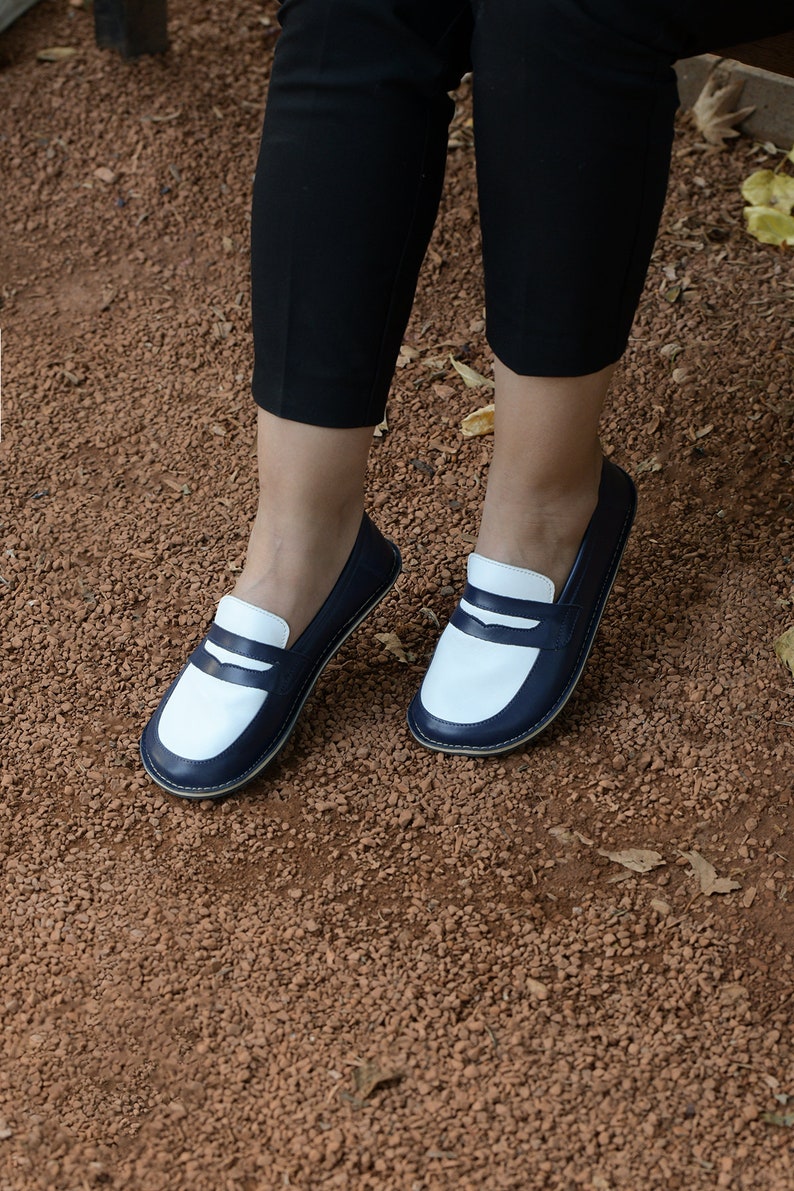 May include: A pair of white and navy blue leather loafers with a contrasting color design. The loafers have a simple, classic style and are perfect for casual wear.