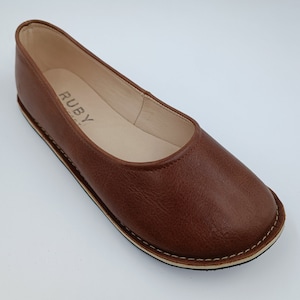 Peut inclure: Ballerine en cuir marron avec un bout arrondi. La chaussure a une semelle cousue et le mot "RUBY" est visible sur la semelle int&eacute;rieure. La chaussure est de couleur marron chaud.