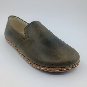 K&ouml;nnte beinhalten: Ein Paar dunkelgr&uuml;ne Lederschuhe zum Reinschl&uuml;pfen mit wei&szlig;en N&auml;hten an der Sohle.