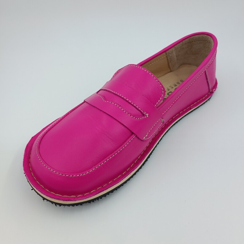 Peut inclure: Un mocassin en cuir rose vif avec des d&eacute;tails de couture blancs et une semelle en caoutchouc noir.