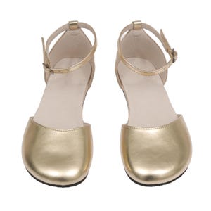 Puede incluir: Un par de sandalias doradas con correas en el tobillo y cierres de hebilla. Las sandalias tienen un dise&ntilde;o de punta redondeada y una plantilla de color neutro. Los zapatos son de material met&aacute;lico brillante.