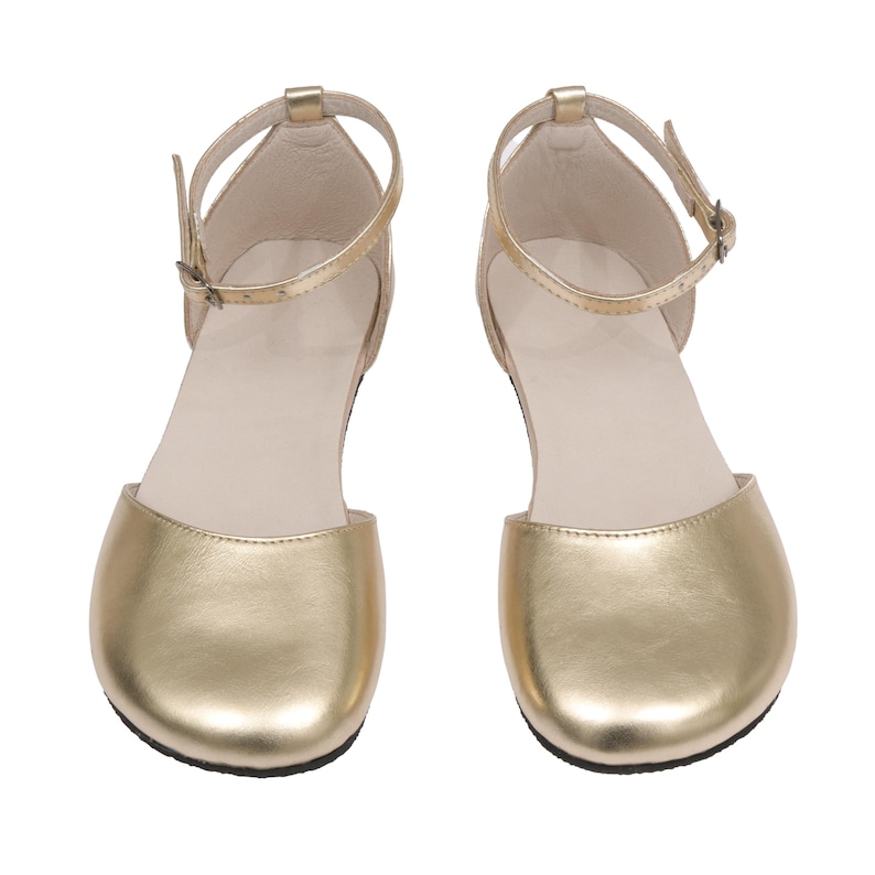 Puede incluir: Un par de sandalias doradas con correas en el tobillo y cierres de hebilla. Las sandalias tienen un dise&ntilde;o de punta redondeada y una plantilla de color neutro. Los zapatos son de material met&aacute;lico brillante.