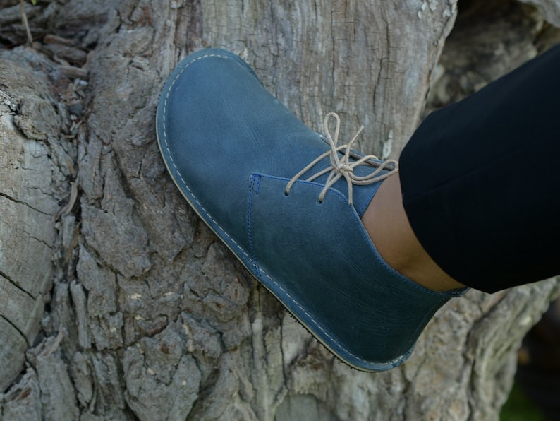 May include: A blue leather ankle boot with a lace-up closure. The boot has a rounded toe and a stitched seam around the sole.