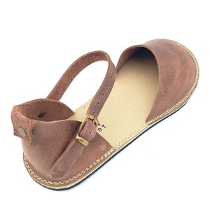 May include: Brown leather sandals with an ankle strap and buckle closure. The sandals have a simple design and a comfortable look.