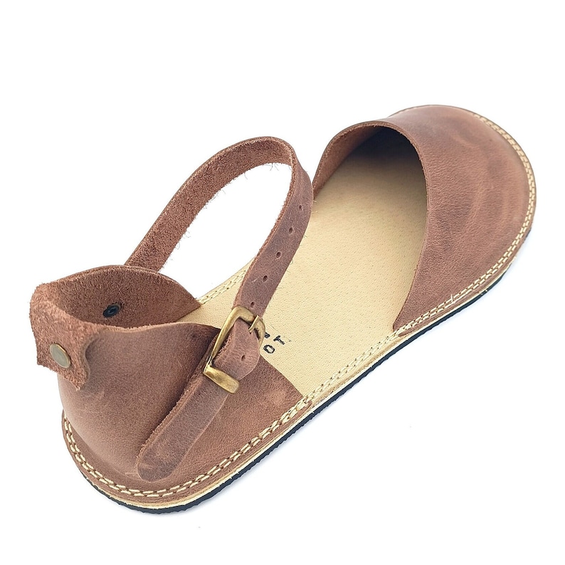 May include: Brown leather sandals with an ankle strap and buckle closure. The sandals have a simple design and a comfortable look.