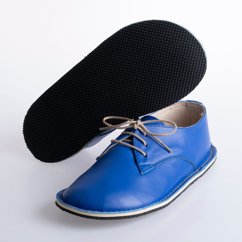 May include: A pair of blue leather lace-up shoes with a white sole and a black rubber outsole. The shoes are shown with one shoe lying on its side, revealing the outsole.
