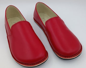 May include: A pair of red leather slip-on shoes with a white stitching detail around the sole. The shoes have a simple design and a comfortable look.