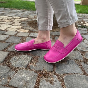 Peut inclure: Une paire de mocassins en cuir rose vif avec une semelle blanche. Les mocassins ont un design classique de mocassin penny avec un d&eacute;tail cousu sur le vamp.