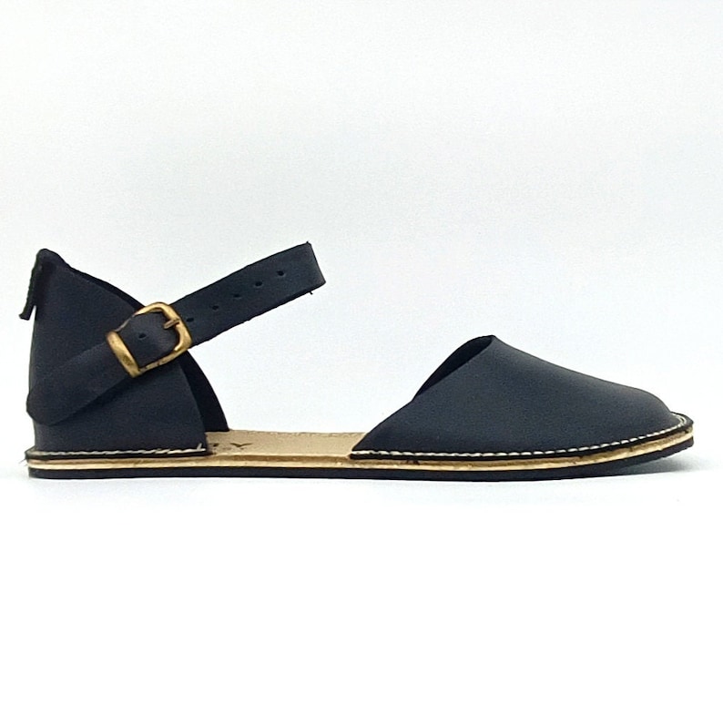 Puede incluir: Sandalias de cuero negro con una correa de tobillo y hebilla. Las sandalias tienen una suela plana y una punta ligeramente puntiaguda.