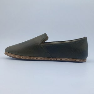 K&ouml;nnte beinhalten: Ein Paar dunkelgr&uuml;ne Lederschuhe zum Hineinschl&uuml;pfen mit braunem Stepprand.