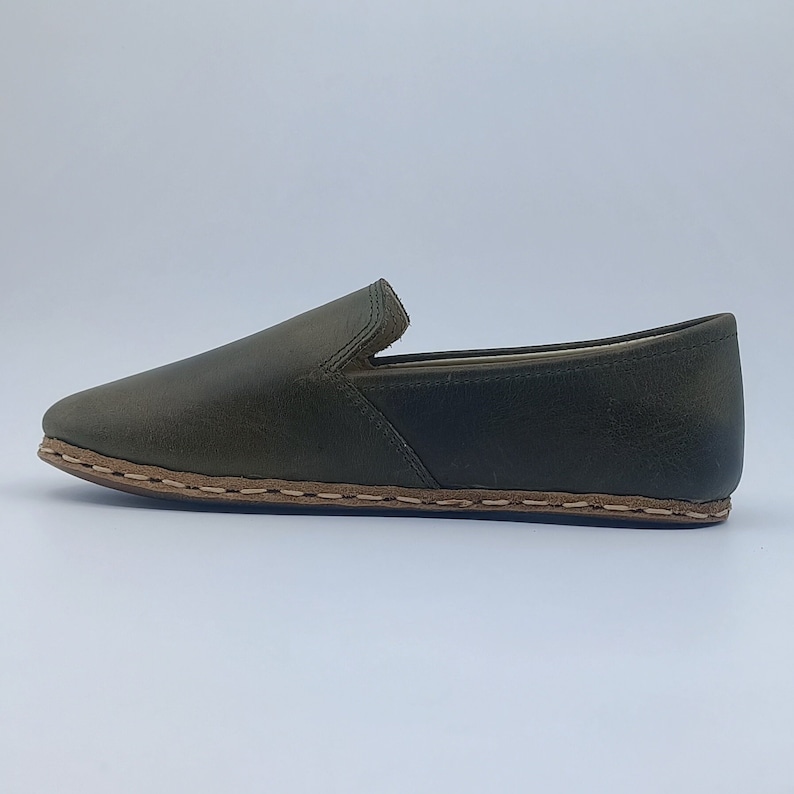 K&ouml;nnte beinhalten: Ein Paar dunkelgr&uuml;ne Lederschuhe zum Hineinschl&uuml;pfen mit braunem Stepprand.
