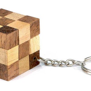 Puede incluir: Un llavero de madera con un rompecabezas de patrón de tablero de ajedrez en tonos de marrón y madera clara. El llavero tiene una cadena de metal plateado y un anillo doble.
