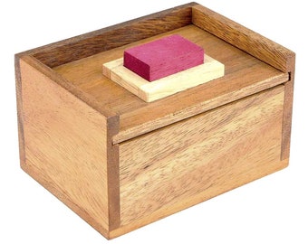 May include: A wooden box puzzle with a sliding lid and a small, red block on top. The box is made of light brown wood and has a natural wood grain.