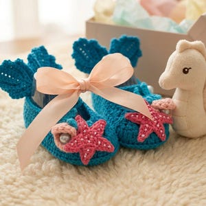 Peut inclure: Chaussons de b&eacute;b&eacute; en crochet turquoise avec des &eacute;toiles de mer roses et un n&oelig;ud en ruban p&ecirc;che. Un jouet hippocampe est &agrave; c&ocirc;t&eacute;. Les chaussons ont un motif de coquillage et sont sur un tapis cr&egrave;me.