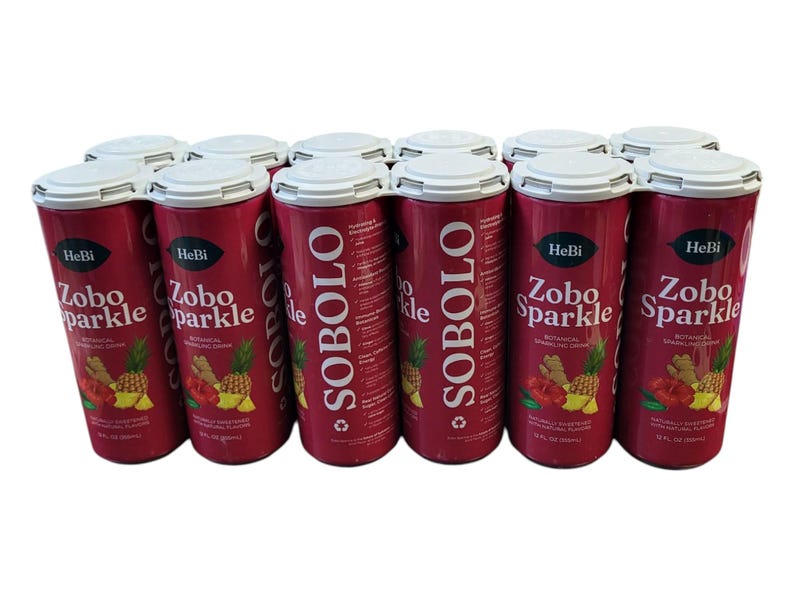 K&ouml;nnte beinhalten: Ein Dutzend Dosen Zobo Sparkle, ein botanisches, prickelndes Getr&auml;nk. Die roten Dosen haben wei&szlig;en Text und Abbildungen von Ananas, Ingwer und Hibiskus. Jede Dose enth&auml;lt 355 ml.