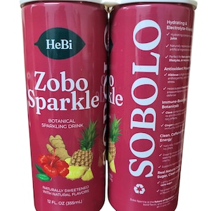 K&ouml;nnte beinhalten: Zwei rote Dosen Zobo Sparkle, ein botanisches Sprudelgetr&auml;nk. Jede Dose zeigt den Markennamen, den Produktnamen und eine Grafik von Hibiskus, Ananas und Ingwer. Die Dosen sind 355 ml.