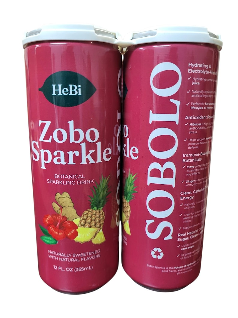 K&ouml;nnte beinhalten: Zwei rote Dosen Zobo Sparkle, ein botanisches Sprudelgetr&auml;nk. Jede Dose zeigt den Markennamen, den Produktnamen und eine Grafik von Hibiskus, Ananas und Ingwer. Die Dosen sind 355 ml.