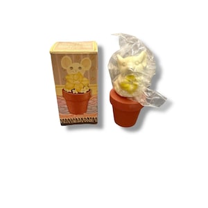 Op de afbeelding: Decoratief muisbeeldje in een terracotta bloempot, met een bijpassende doos. De muis is wit met gele accenten. De doos heeft een vergelijkbaar ontwerp met een muis en een bloempot.