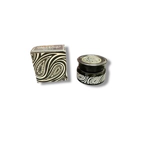 May include: A black and white jar and box set featuring a paisley pattern. The jar has a black lid and base with a white paisley design. The box is black and white with the same paisley pattern. The text on the box reads "Patterns Organic Basket".