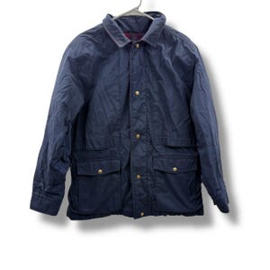 May include: A navy blue jacket with a collared neckline and four front pockets. The jacket has gold-colored buttons and is hanging on a metal hanger. The jacket appears to be made of a durable, water-resistant material.