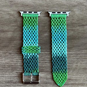 May include: A two-piece watch band featuring a woven macrame design with an ombre color gradient transitioning from light green to turquoise and dark forest green. The band includes silver-toned metal connectors and a silver-toned metal buckle.