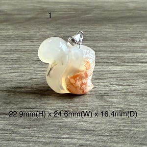 May include: A white and orange agate pendant carved in the shape of a squirrel. The pendant is approximately 22.9 mm high, 24.6 mm wide, and 16.4 mm deep.
